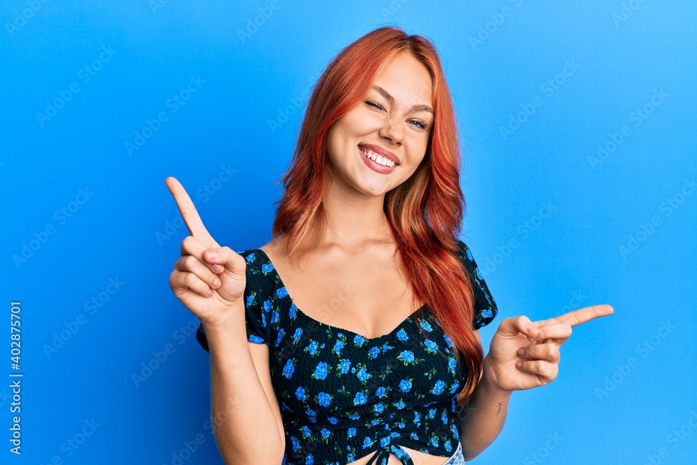 Young beautiful redhead woman wearing casual clothes over blue background smiling confident pointing with fingers to different directions. copy space for advertisement Young beautiful redhead woman wearing casual clothes over blue background smiling confident pointing with fingers to different directions. copy space for advertisement