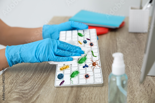 Woman cleaning computer keayboard from microbes at table in office, closeup