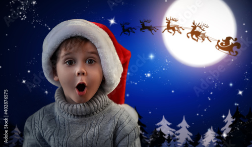 Cute little child and Santa Claus flying in his sleigh against moon sky on background. Christmas celebration © New Africa