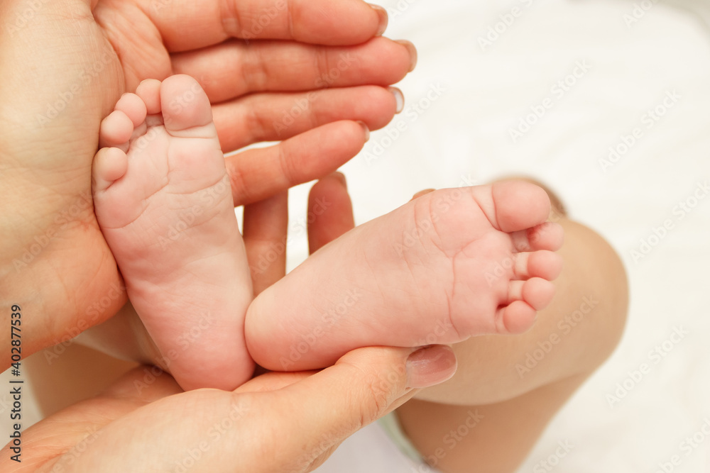 Hands of woman holds baby foot, blurred background Hands of woman holds baby foot, blurred background