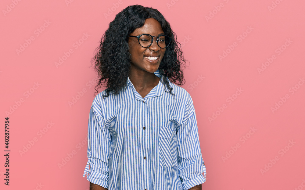 Beautiful african young woman wearing casual clothes and glasses winking looking at the camera with sexy expression, cheerful and happy face. Beautiful african young woman wearing casual clothes and glasses winking looking at the camera with sexy expression, cheerful and happy face.