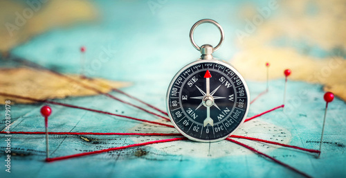 Magnetic compass  and location marking with a pin on routes on world map. Adventure, discovery, navigation, communication, logistics, geography and travel theme concept background.. Macro photo. photo