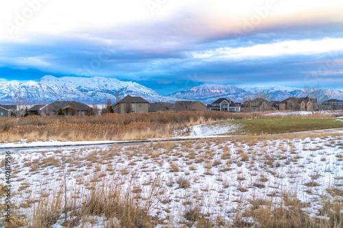 Vast grassy terrain in the valley dusted with snow against homes and mountain
