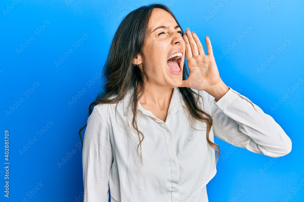 Young brunette woman wearing casual clothes shouting and screaming loud to side with hand on mouth. communication concept.
