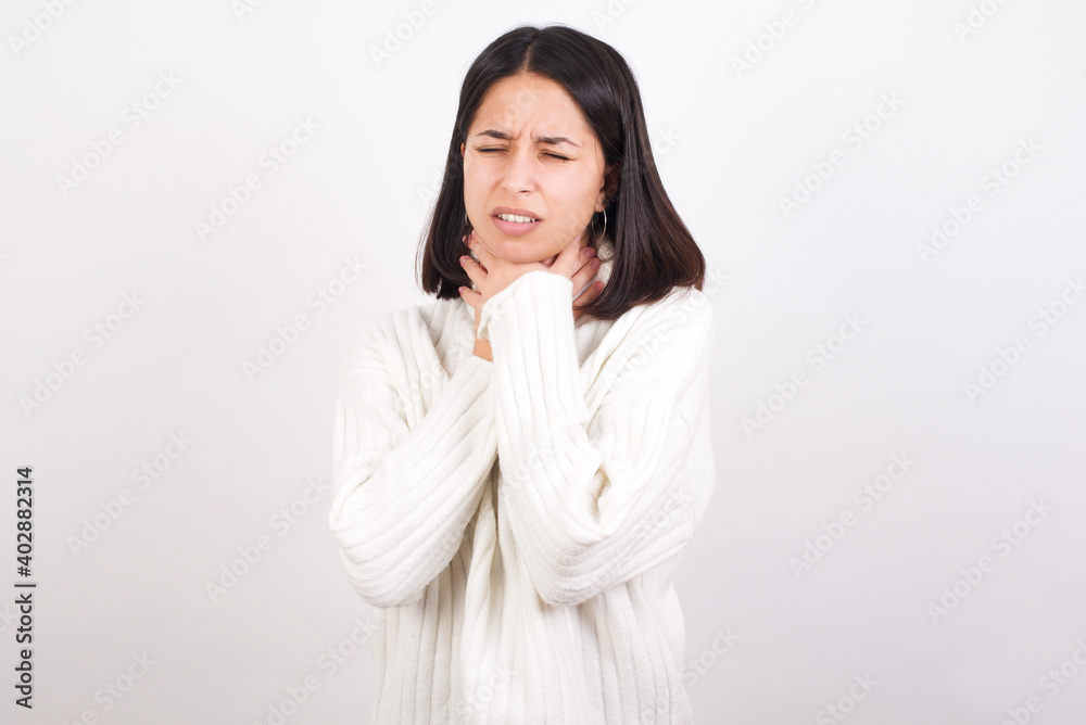 Young brunette woman wearing white knitted sweater against white background shouting suffocate because painful strangle. Health problem. Asphyxiate and suicide concept. Young brunette woman wearing white knitted sweater against white background shouting suffocate because painful strangle. Health problem. Asphyxiate and suicide concept.