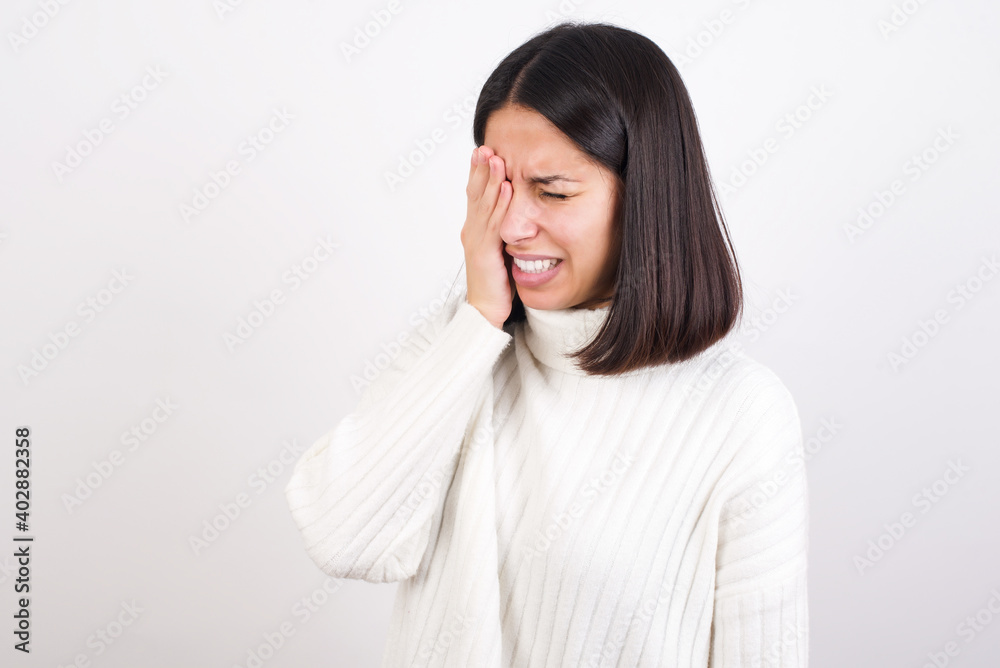 Young brunette woman wearing white knitted sweater against white background Yawning tired covering half face, eye and mouth with hand. Face hurts in pain. Young brunette woman wearing white knitted sweater against white background Yawning tired covering half face, eye and mouth with hand. Face hurts in pain.