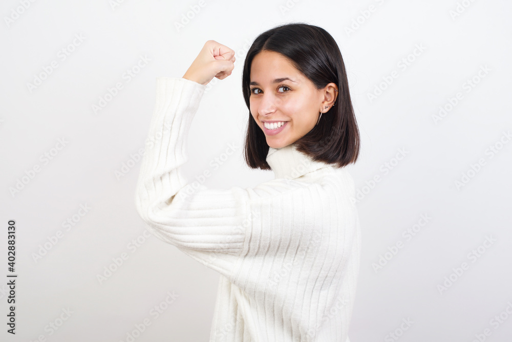 Portrait of powerful cheerful Young brunette woman wearing white knitted sweater against white background showing muscles. Portrait of powerful cheerful Young brunette woman wearing white knitted sweater against white background showing muscles.