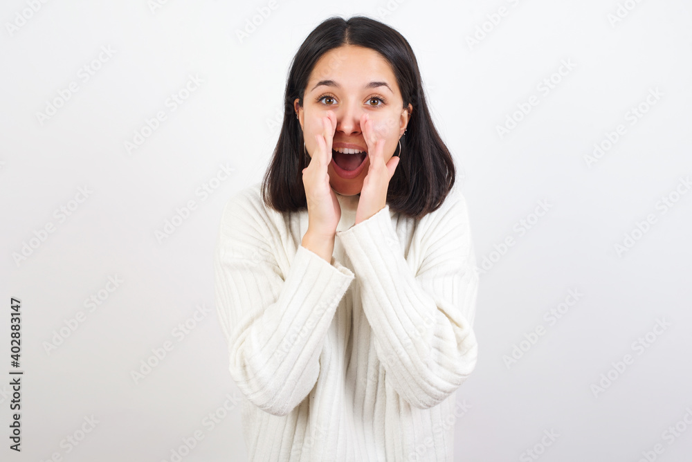 Young brunette woman wearing white knitted sweater against white background shouting excited to front. Young brunette woman wearing white knitted sweater against white background shouting excited to front.