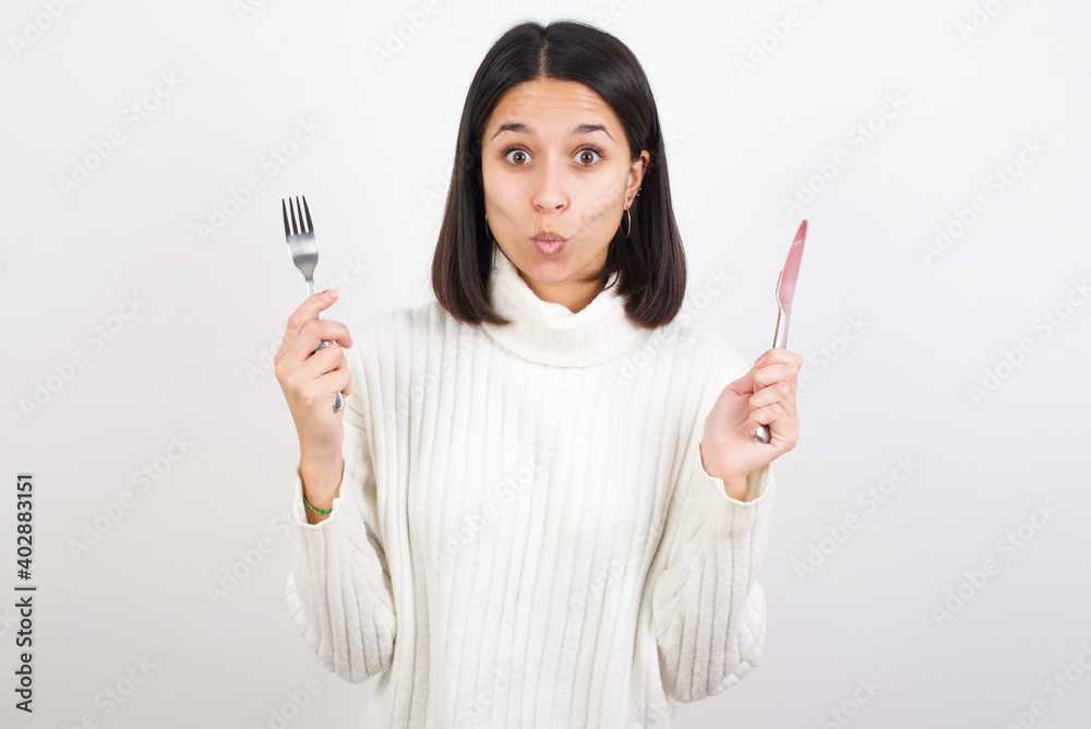 Model hungry Young brunette woman wearing white knitted sweater against white background holding in hand fork knife want tasty yummy pizza pie Model hungry Young brunette woman wearing white knitted sweater against white background holding in hand fork knife want tasty yummy pizza pie