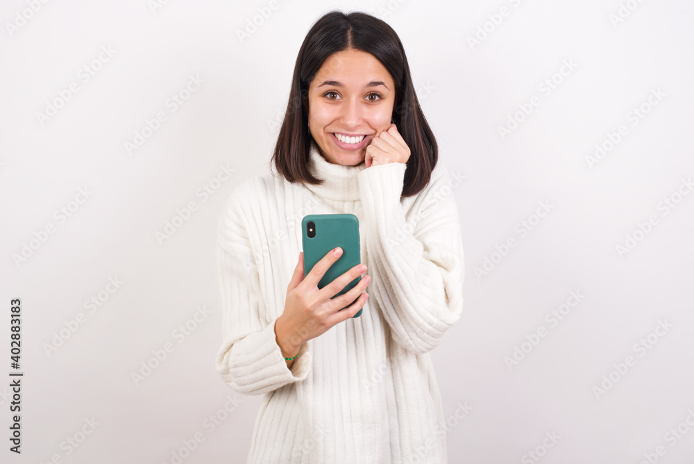 Joyous Young brunette woman wearing white sweater poses with mobile phone device, types text message on modern smartphone, watches funny video during free time, enjoys good internet connection, Joyous Young brunette woman wearing white sweater poses with mobile phone device, types text message on modern smartphone, watches funny video during free time, enjoys good internet connection,