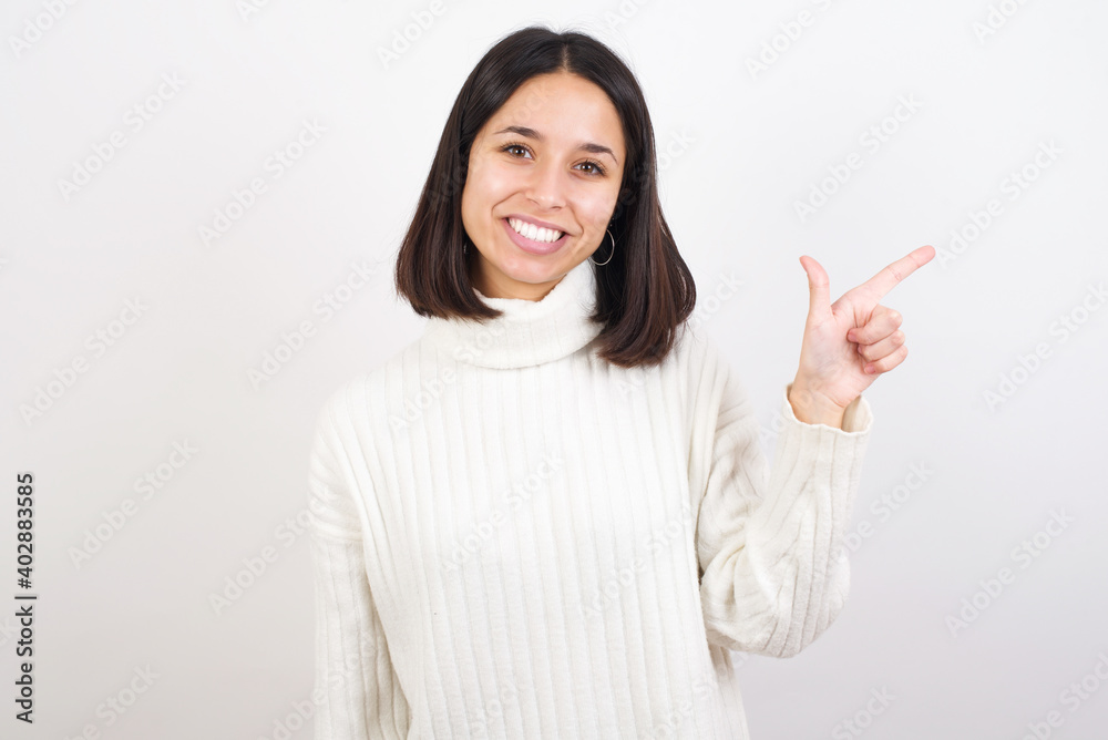 Young brunette woman wearing white knitted sweater against white background pointing up with fingers number eight in Chinese sign language BÄ. Young brunette woman wearing white knitted sweater against white background pointing up with fingers number eight in Chinese sign language BÄ.