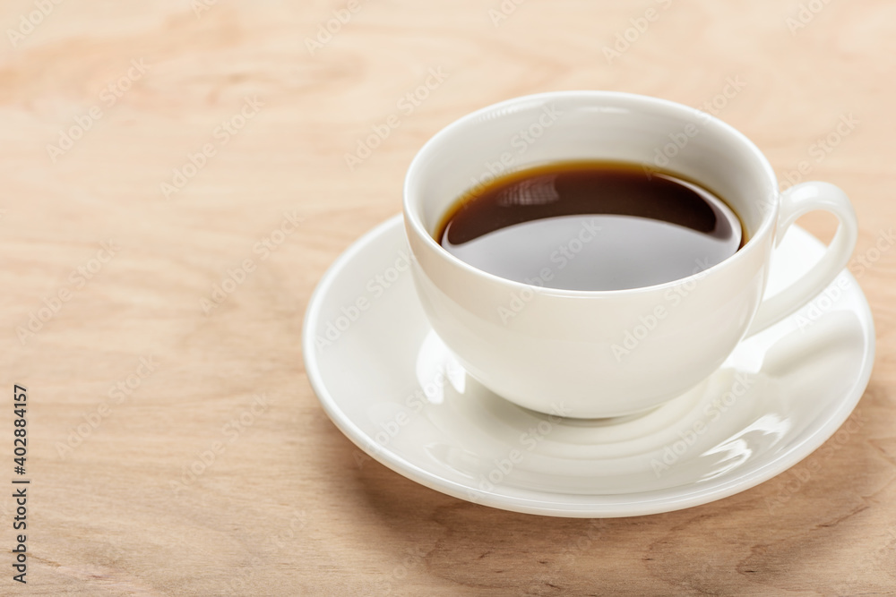 White cup with a beverage on a saucer on a wooden table.