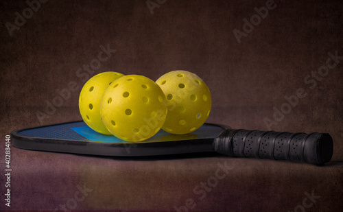 A pickleball paddle and three pickleballs over a dark background. The sport of pickleball is America's fastest growing sport. © justasc