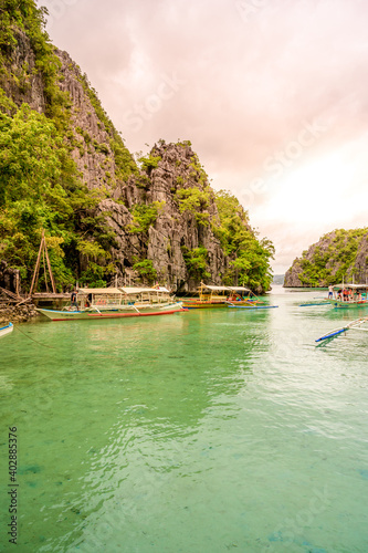 Blue crystal water in paradise Bay with boats on the wooden pier at Kayangan Lake in Coron island, tropical travel destination - Palawan, Philippines.