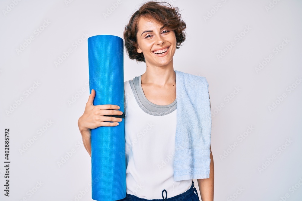 Young hispanic woman holding yoga mat looking positive and happy standing and smiling with a confident smile showing teeth Young hispanic woman holding yoga mat looking positive and happy standing and smiling with a confident smile showing teeth