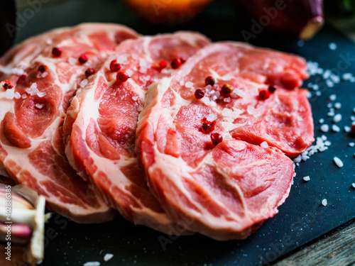 Raw pork chops with onion garlic and seasonings on plate on wooden table 