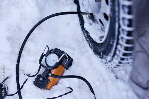 car pump compressor pumps up a flat tire of a car in winter on a snowy path in the forest close-up. Broken cars concept.