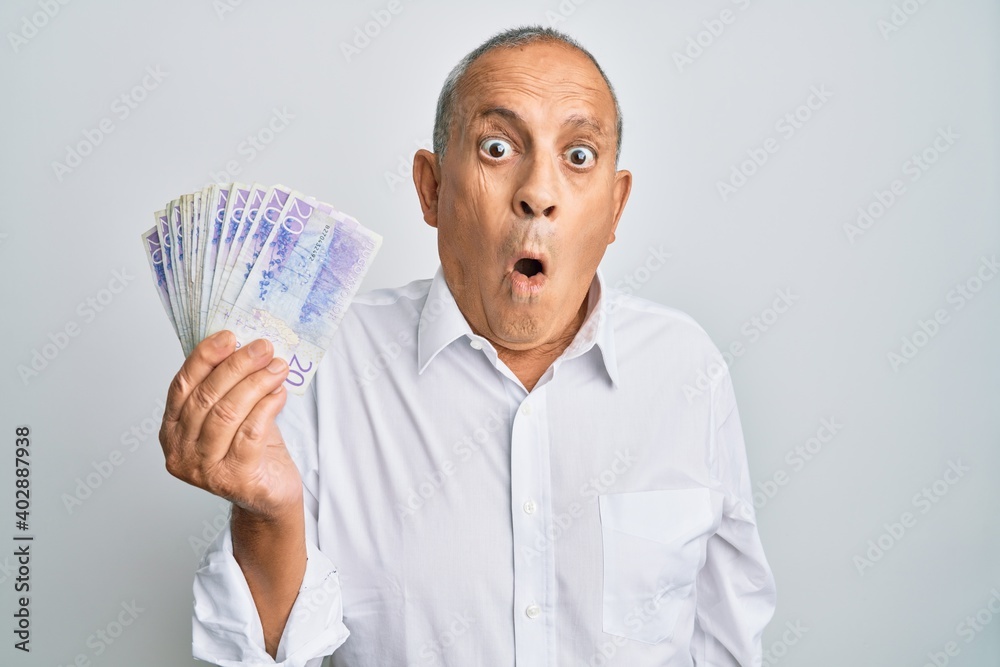 Handsome senior man holding 20 swedish krona banknotes scared and amazed with open mouth for surprise, disbelief face Handsome senior man holding 20 swedish krona banknotes scared and amazed with open mouth for surprise, disbelief face
