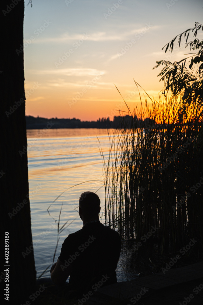 Fototapeta premium sunset and burning sun over the river and a man looking beyond the horizon