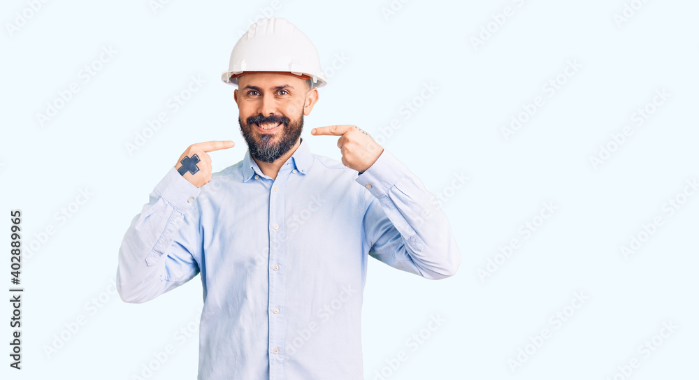 Young handsome man wearing architect hardhat smiling cheerful showing and pointing with fingers teeth and mouth. dental health concept. Young handsome man wearing architect hardhat smiling cheerful showing and pointing with fingers teeth and mouth. dental health concept.