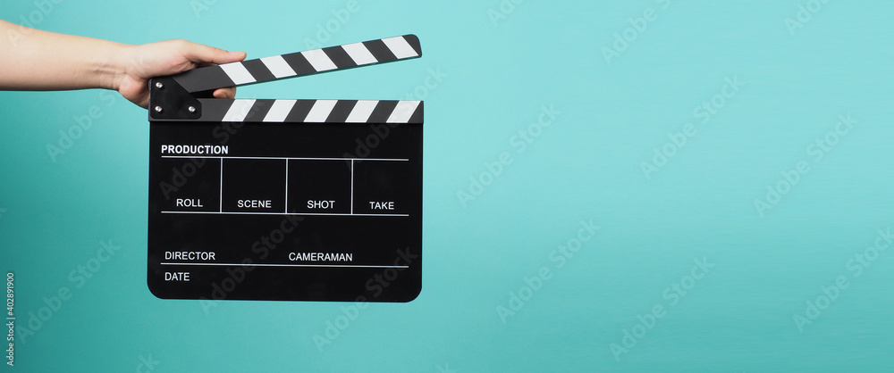 Hand is holding Black clapper board or movie slate on pastel blue or Tiffany Blue background.