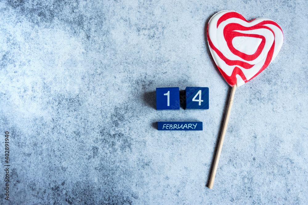 Top view of 14 February lettering and a heart-shaped lollypop on grey concrete background, copy space