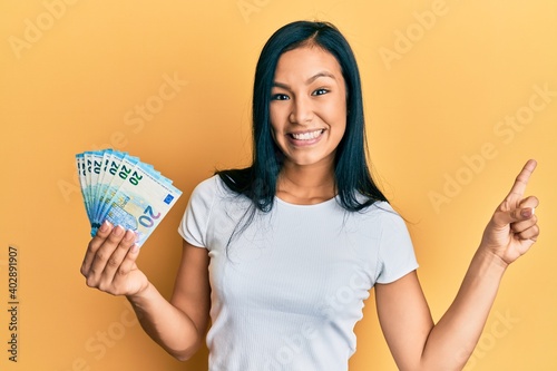 Beautiful hispanic woman holding 20 euros banknotes smiling happy pointing with hand and finger to the side