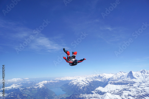 Skydivers perform tricks above snowcapped mountains