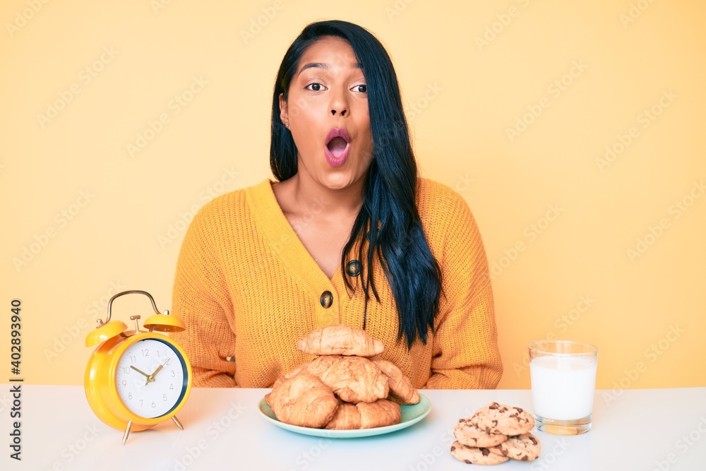 Beautiful latin young woman with long hair sitting on the table having breakfast scared and amazed with open mouth for surprise, disbelief face Beautiful latin young woman with long hair sitting on the table having breakfast scared and amazed with open mouth for surprise, disbelief face