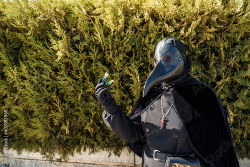 plague doctor holds a vaccine against a background of plants