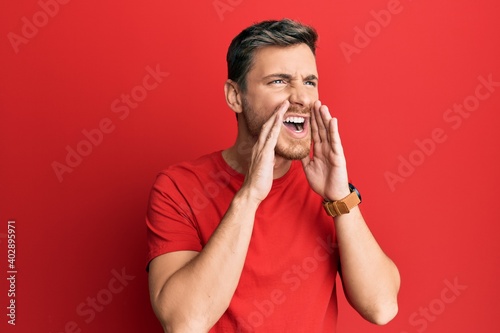 Handsome caucasian man wearing casual red tshirt shouting angry out loud with hands over mouth © Krakenimages.com