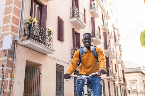 Black Man Riding Bike Wearing Yellow Sweater Outdoors. © MCStock