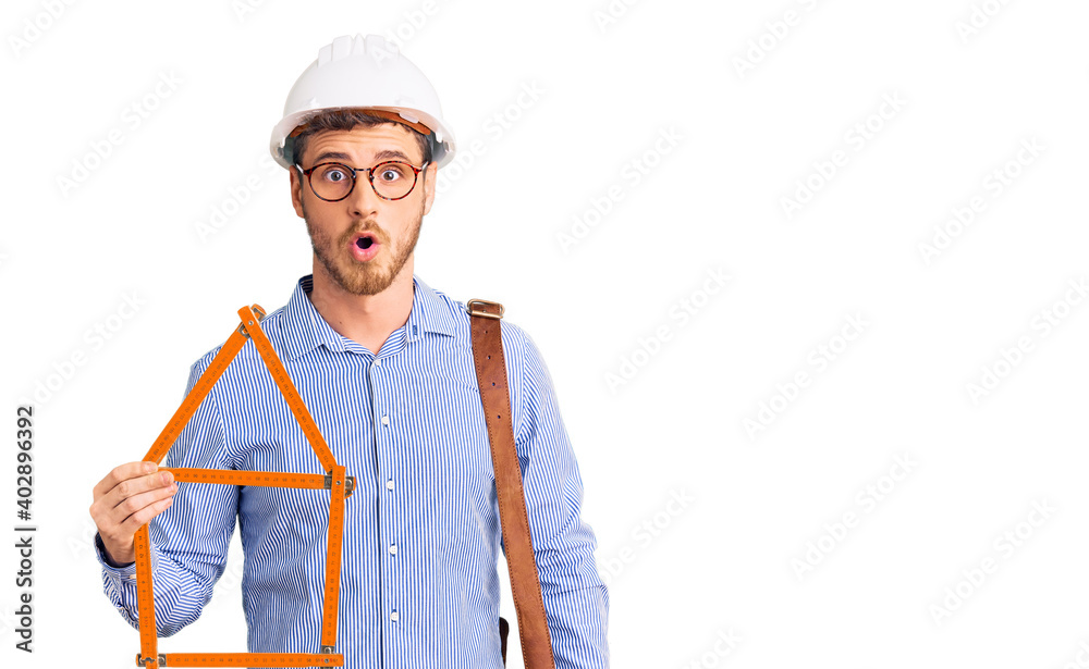 Handsome young man with bear wearing architect hardhat holding build project scared and amazed with open mouth for surprise, disbelief face Handsome young man with bear wearing architect hardhat holding build project scared and amazed with open mouth for surprise, disbelief face