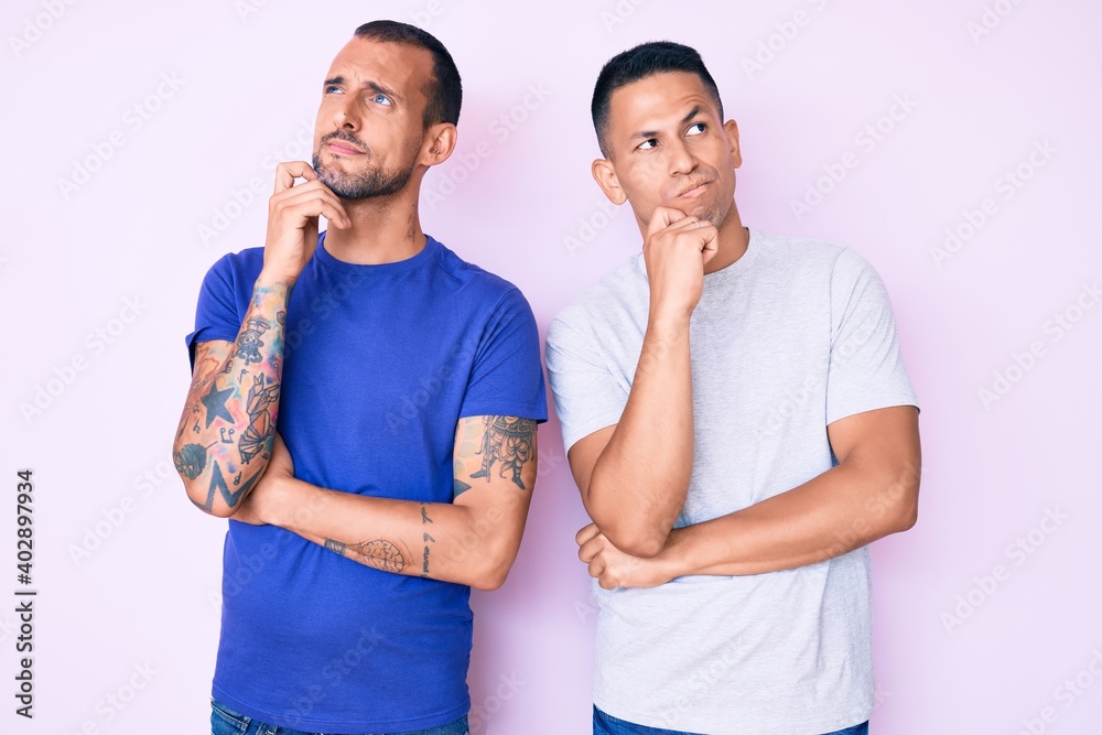 Naklejka premium Young gay couple of two men wearing casual clothes serious face thinking about question with hand on chin, thoughtful about confusing idea