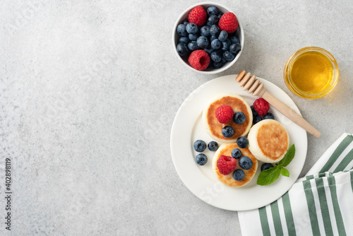 Cottage cheese fritters with summer berries and honey. Top view, grey concrete background with copy space
