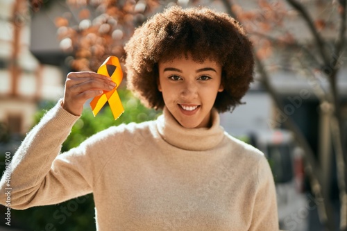 Young hispanic girl smiling happy holding orange awareness ribbon at the city.