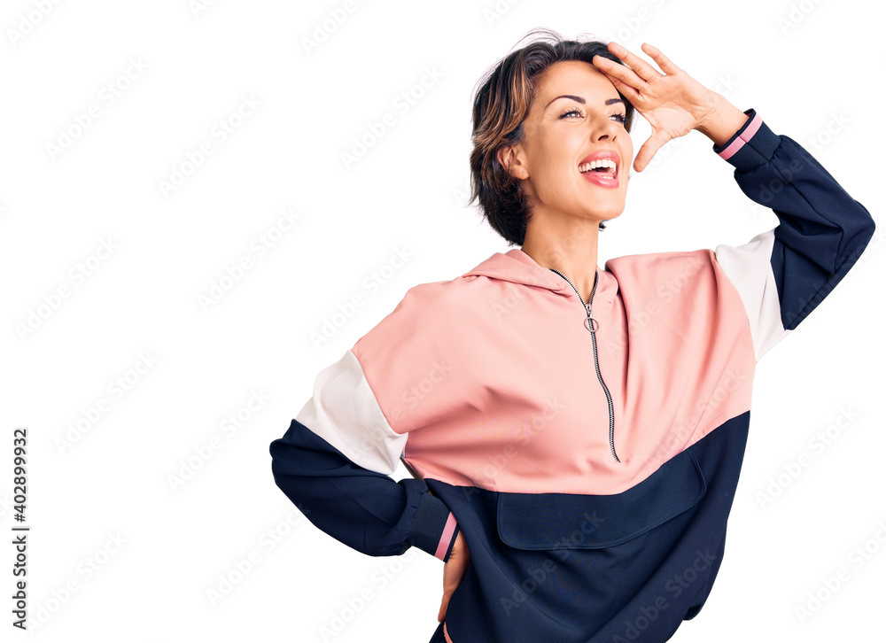 Young beautiful woman wearing sportswear very happy and smiling looking far away with hand over head. searching concept. Young beautiful woman wearing sportswear very happy and smiling looking far away with hand over head. searching concept.