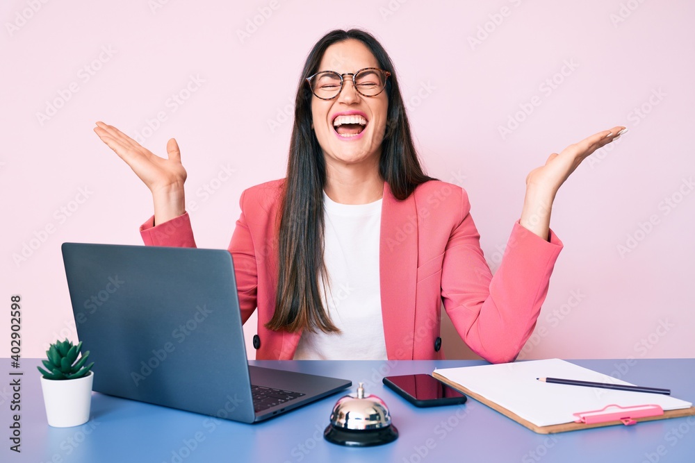 Young caucasian woman sitting at the recepcionist desk working using laptop celebrating mad and crazy for success with arms raised and closed eyes screaming excited. winner concept Young caucasian woman sitting at the recepcionist desk working using laptop celebrating mad and crazy for success with arms raised and closed eyes screaming excited. winner concept