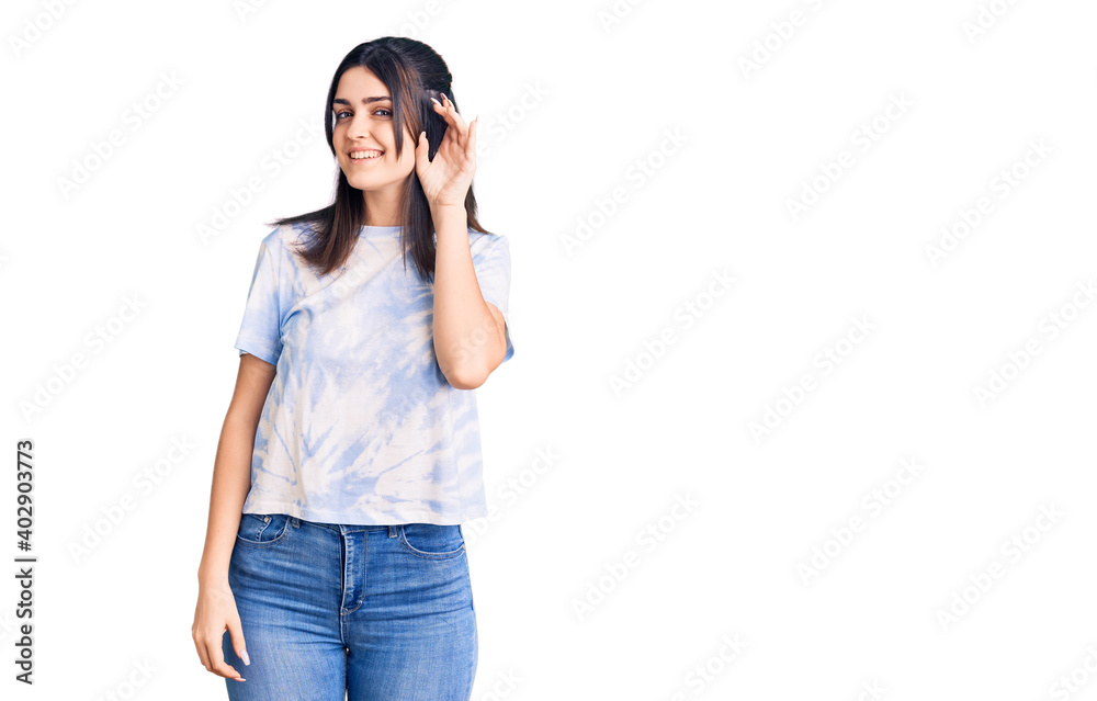 Young beautiful girl wearing casual t shirt smiling with hand over ear listening an hearing to rumor or gossip. deafness concept. Young beautiful girl wearing casual t shirt smiling with hand over ear listening an hearing to rumor or gossip. deafness concept.