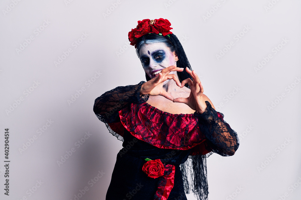 Young woman wearing mexican day of the dead makeup smiling in love doing heart symbol shape with hands. romantic concept. Young woman wearing mexican day of the dead makeup smiling in love doing heart symbol shape with hands. romantic concept.