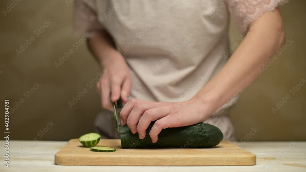 Woman slicing cucumber on kitchen board, no face Woman slicing cucumber on kitchen board, no face
