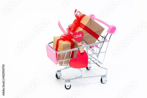Small grocery cart with gift boxes on white background. Give gifts with love on Valentine's Day, Christmas and birthday. Shopping online. Holiday sales and discounts. Retail and wholesale purchases