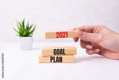 Businessman hand holding wooden cube with text 2021 GOAL, PLAN and ACTION on table background. Resolution, strategy, solution, goal, business and New Year holiday concepts