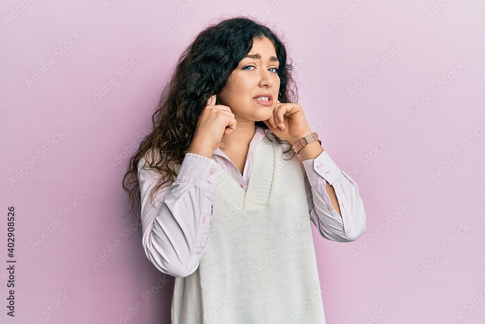 Young brunette woman with curly hair wearing casual clothes covering ears with fingers with annoyed expression for the noise of loud music. deaf concept. Young brunette woman with curly hair wearing casual clothes covering ears with fingers with annoyed expression for the noise of loud music. deaf concept.