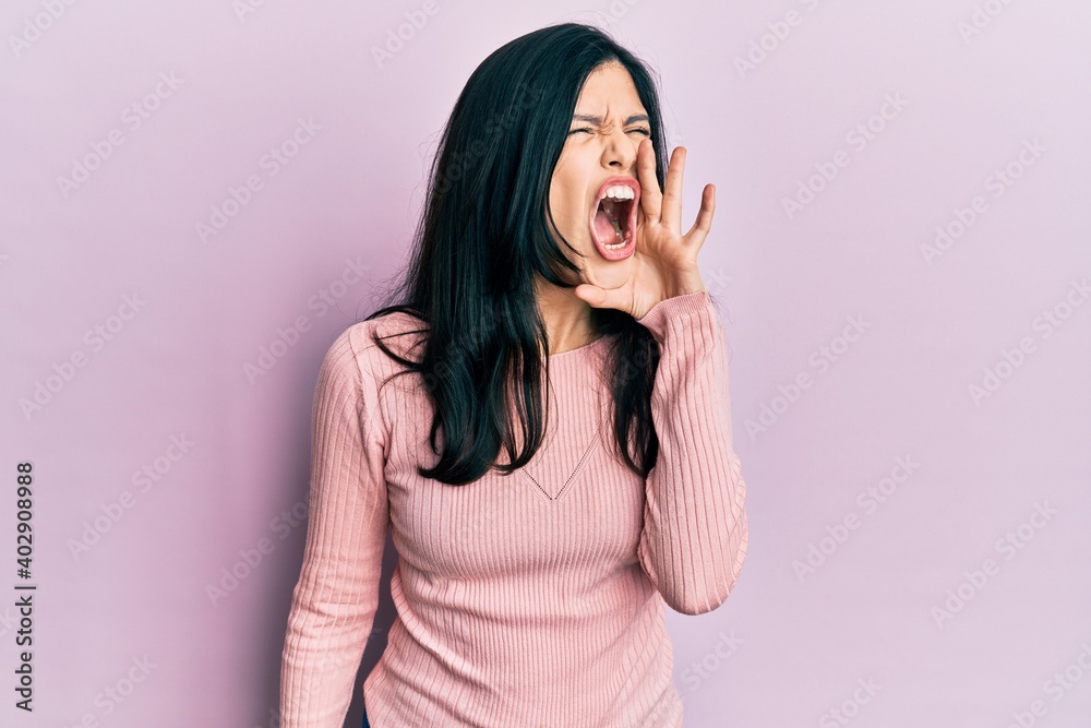 Young hispanic woman wearing casual clothes shouting and screaming loud to side with hand on mouth. communication concept. Young hispanic woman wearing casual clothes shouting and screaming loud to side with hand on mouth. communication concept.
