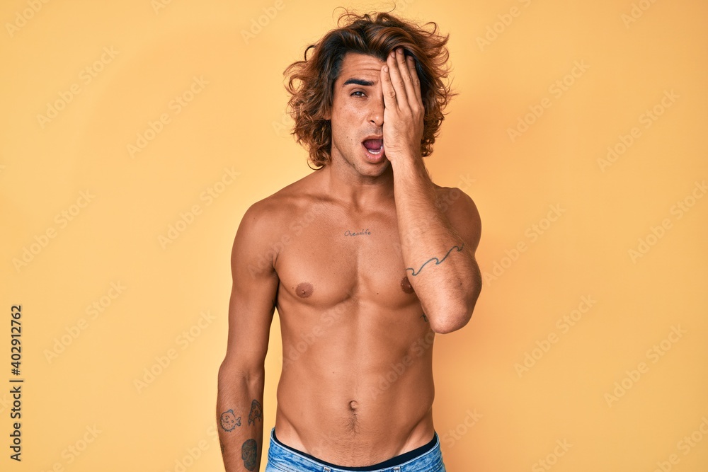 Young hispanic man standing shirtless yawning tired covering half face, eye and mouth with hand. face hurts in pain.