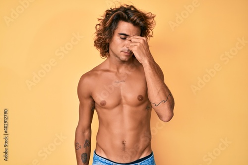 Young hispanic man standing shirtless tired rubbing nose and eyes feeling fatigue and headache. stress and frustration concept.