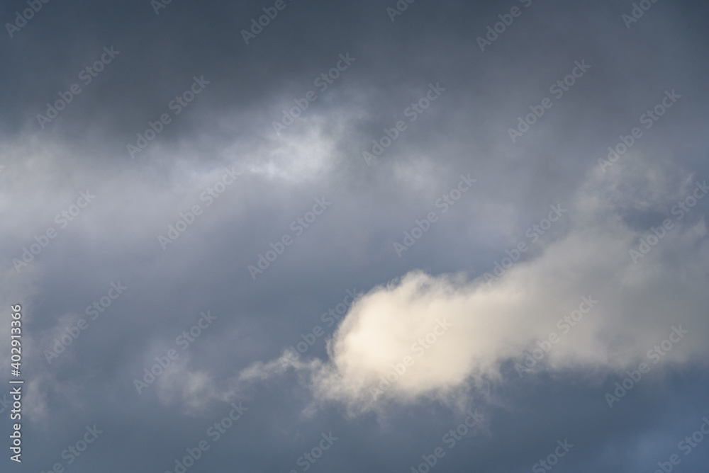 Stormy gray skies with one cloud highlighted white by the sun, as a nature background
