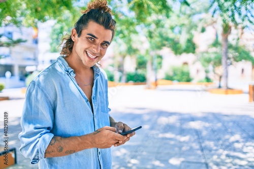 Young hispanic man smiling happy using smartphone at street of city