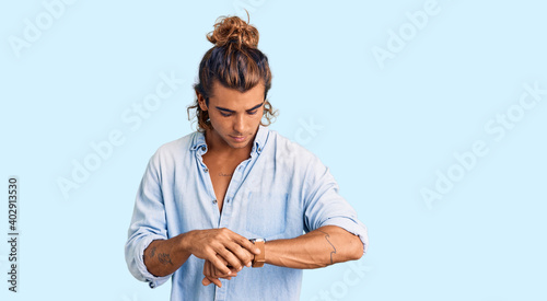 Young hispanic man wearing summer style checking the time on wrist watch, relaxed and confident